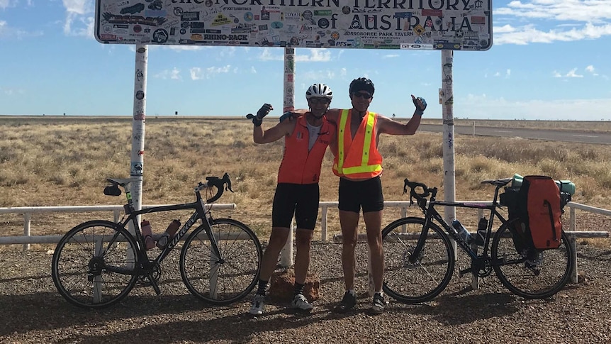Ross Andrewartha and another person stand under the 'Welcome to the Northern Territory sign