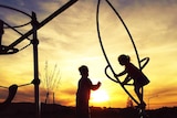 Two unidentified children in a playground at sunset