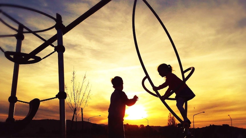 Two unidentified children in a playground at sunset