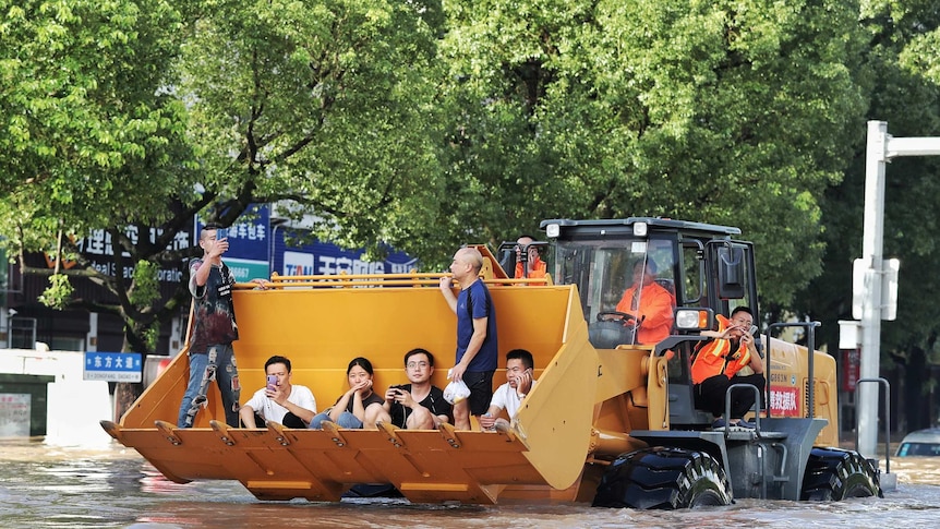 People sit on a bulldozer's shovel as they are ferried down a flooded street in China.