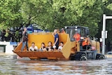 People sit on a bulldozer's shovel as they are ferried down a flooded street in China.