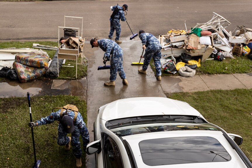 People in blue air force uniforms sweep a driveway that's covered in mud
