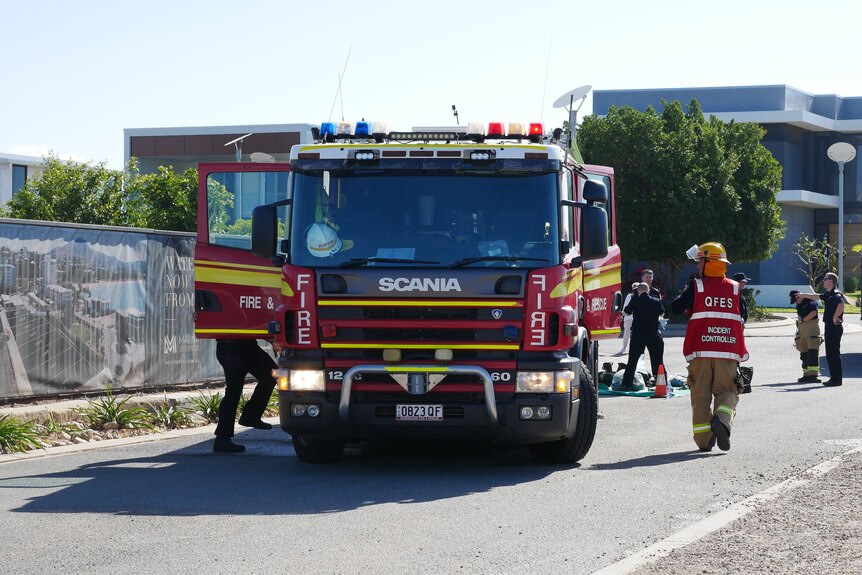 Uniformed fire fighters standing around a fire truck in an outdoor car park.