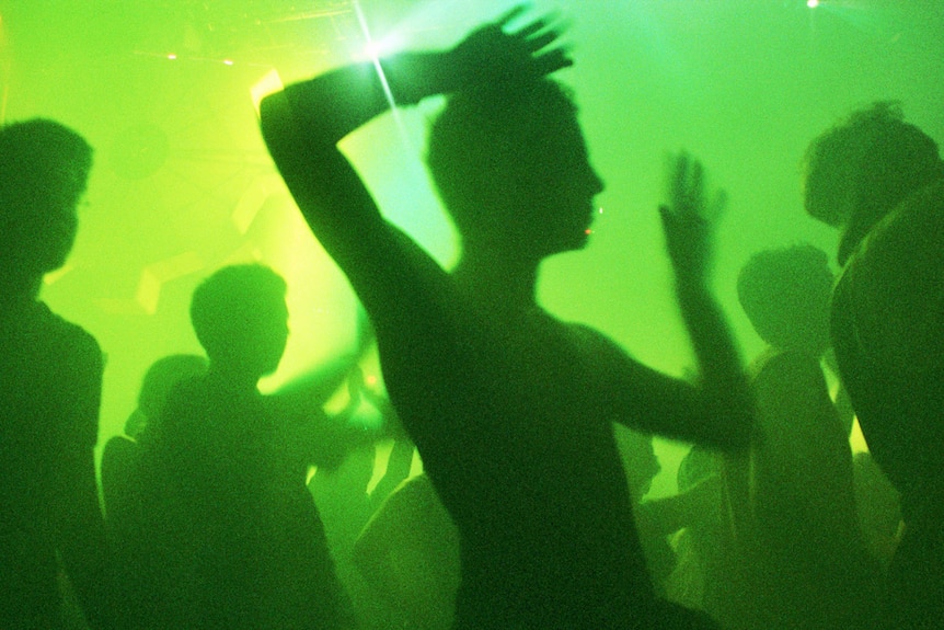 A person in silhouette dances with their hands in the air