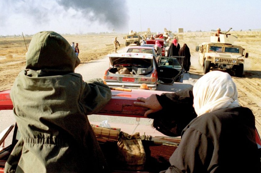 Still from the 2009 film Son of Babylon set in Iraq, featuring queue of cars, men on trucks and smoke in the distance.