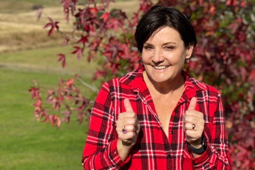 a woman in front of a tree with her thumbs up