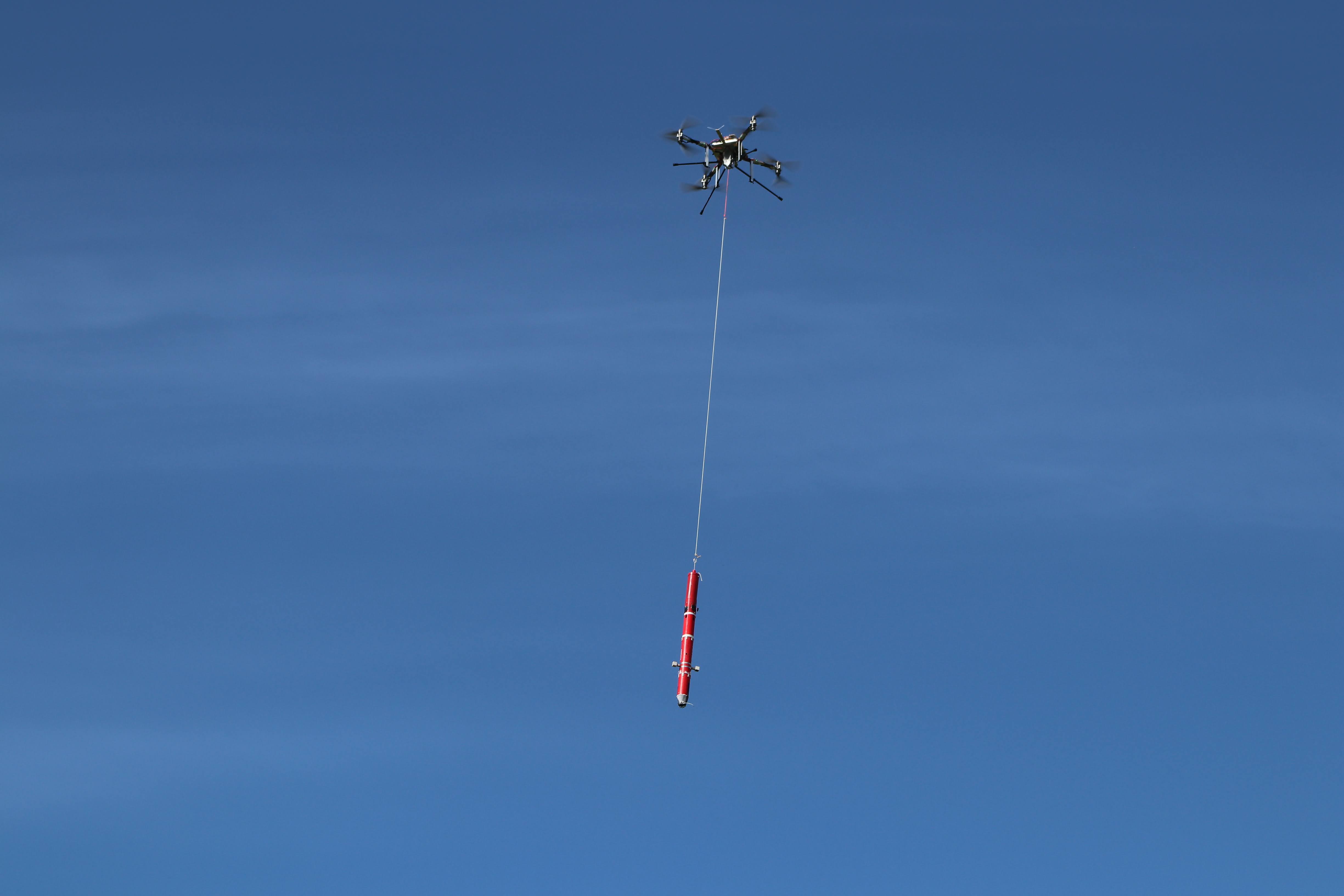 A drone carrying a device on a rope in the sky.