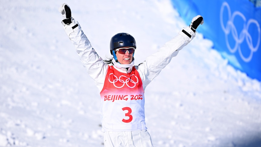 Laura Peel holds her arms in the air and smiles as she skis at the bottom of the hill