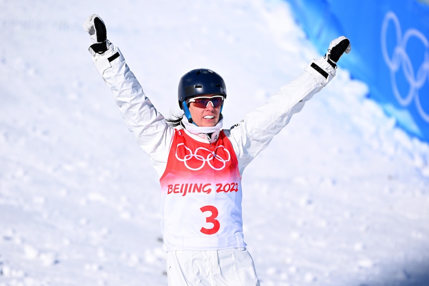 Laura Peel holds her arms in the air and smiles as she skis at the bottom of the hill