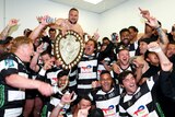 A New Zealand regional rugby union team smile and shout in the dressing room as they spray alcohol near the trophy after a win.