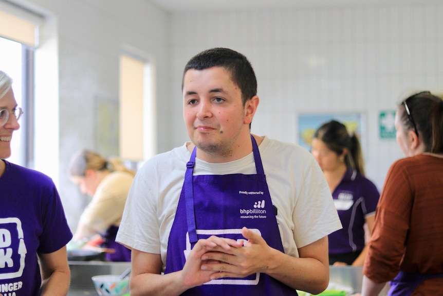 A young man wearing a white t-shirt and a purple apron.