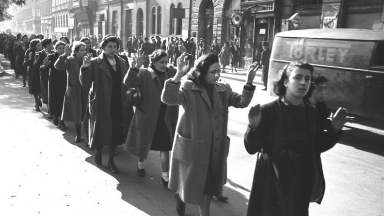 A black and white photo of captured Jewish women with their hands up.