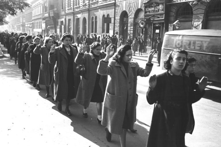 A black and white photo of captured Jewish women with their hands up.