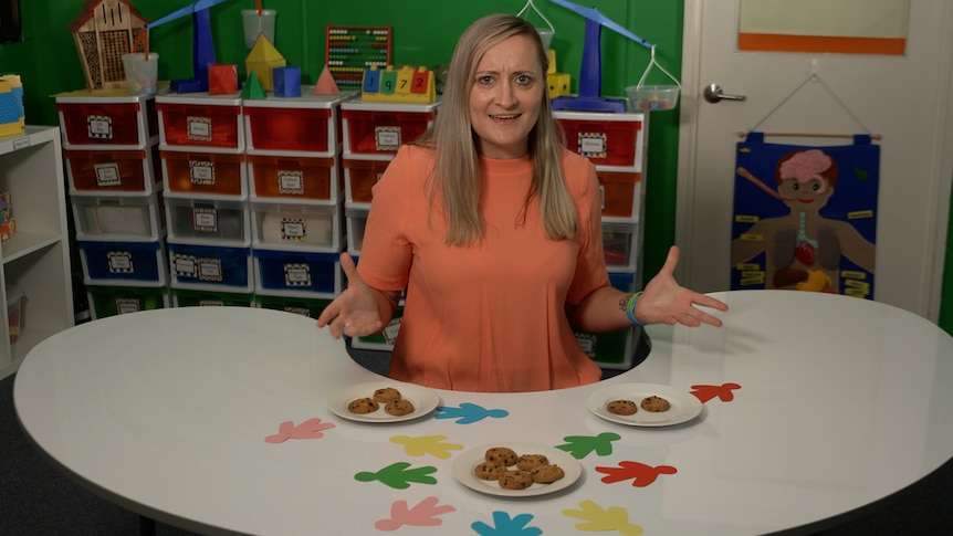Female teacher stands in classroom in front of table with plates of cookies