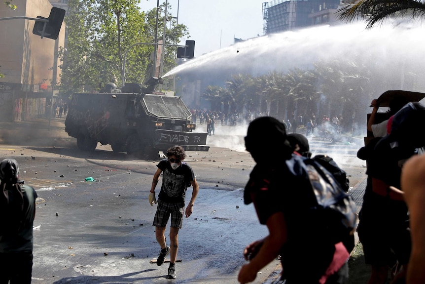 A police truck sprays water canons at protesters wearing mouth masks.