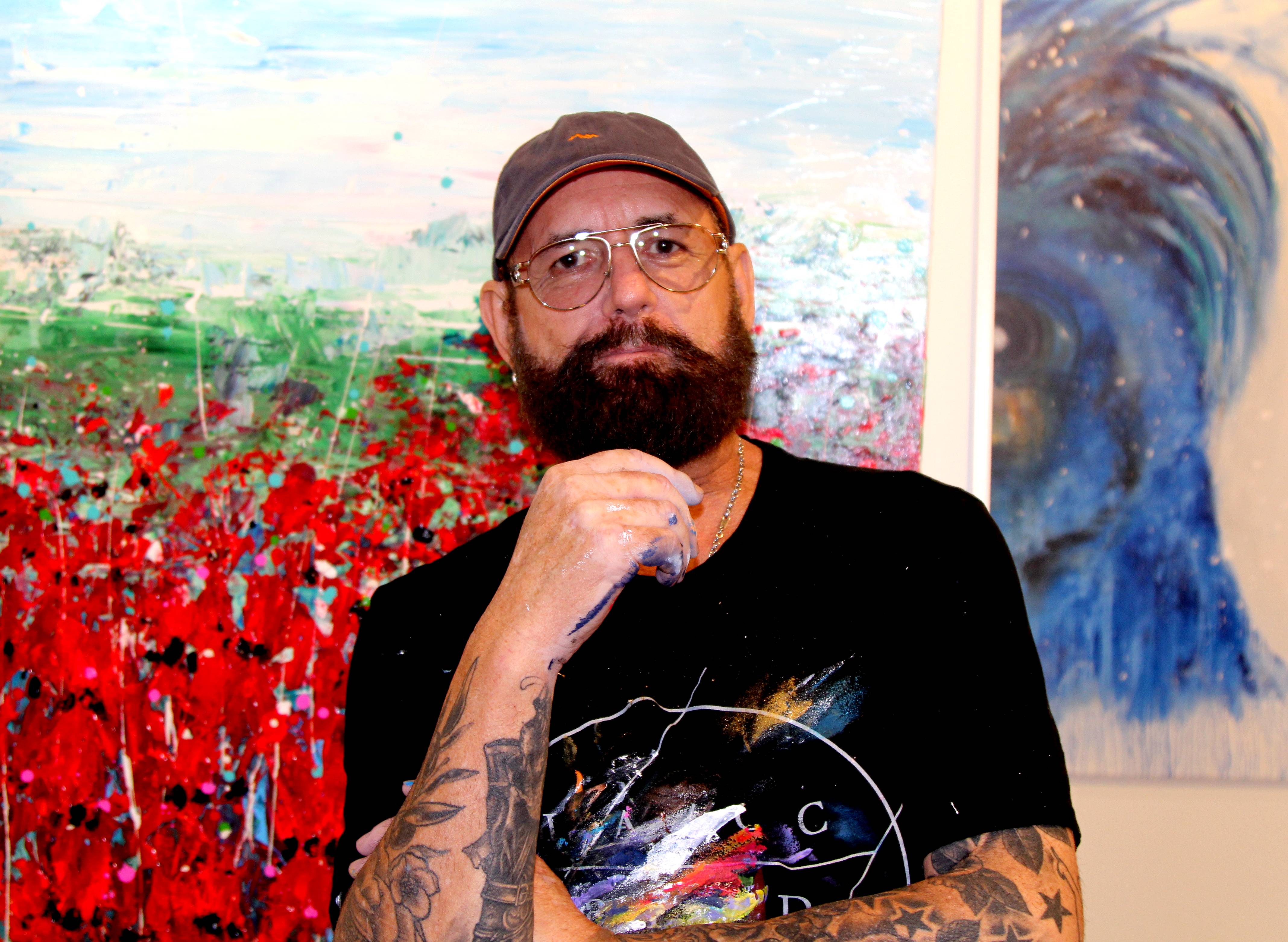 Adelaide artist Mark Lobert stands in front of paintings.