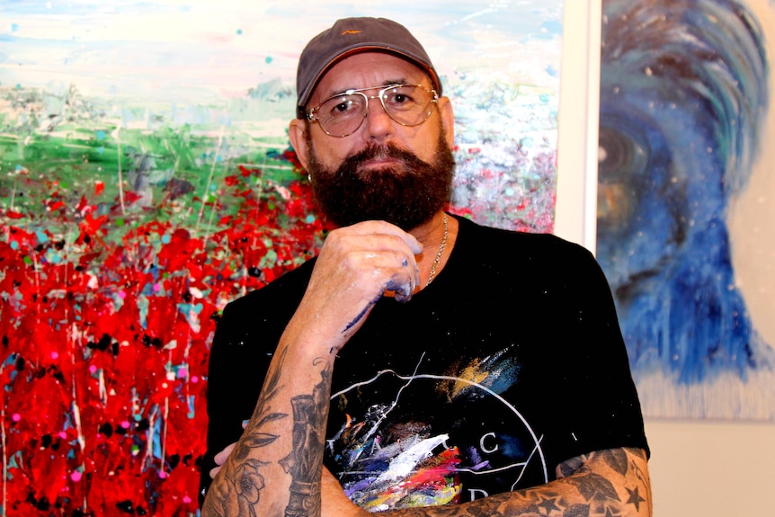 Adelaide artist Mark Lobert stands in front of paintings.