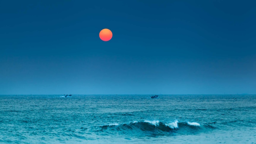The Taiwan strait photographed at dusk with a bright sun setting and fishboats on the water