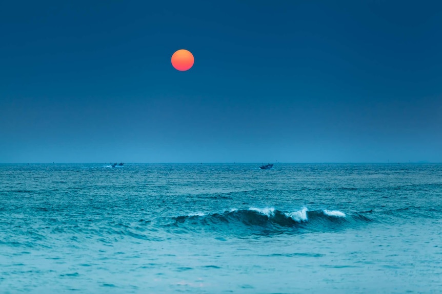 The Taiwan strait photographed at dusk with a bright sun setting and fishboats on the water