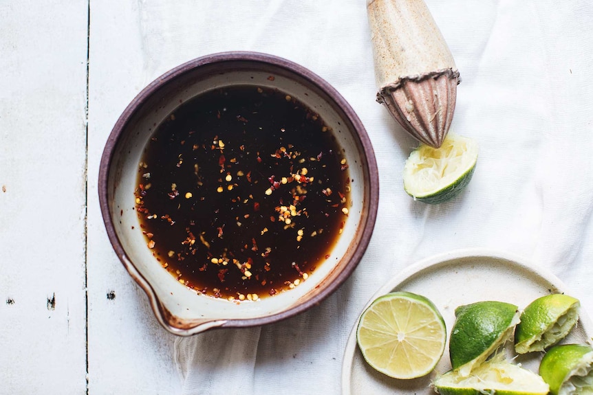 A bowl of soy sauce with chilli flakes and a plate full of limes make a vegan fish sauce for pad thai salad recipe.