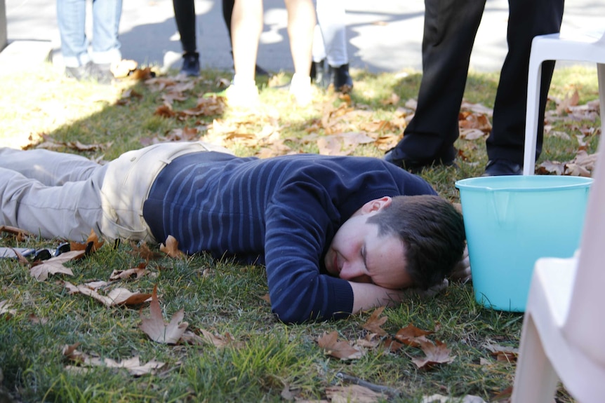 A man lies on the ground with a bucket.