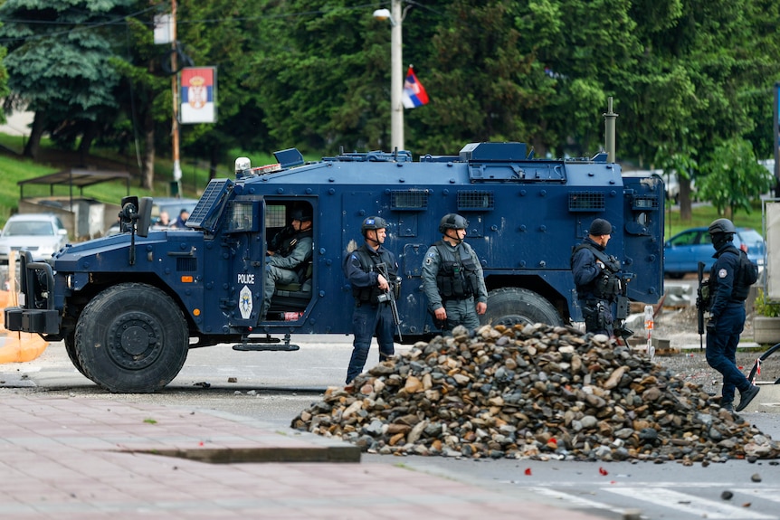 Police stand next to an armoured vehicle near a pile of stones.