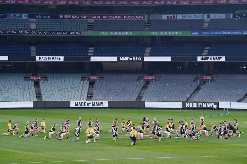 Players from two AFL teams go on one knee in the centre circle ahead of their match at the MCG.