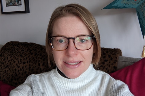 A woman sits on a couch, smiling at the camera. 