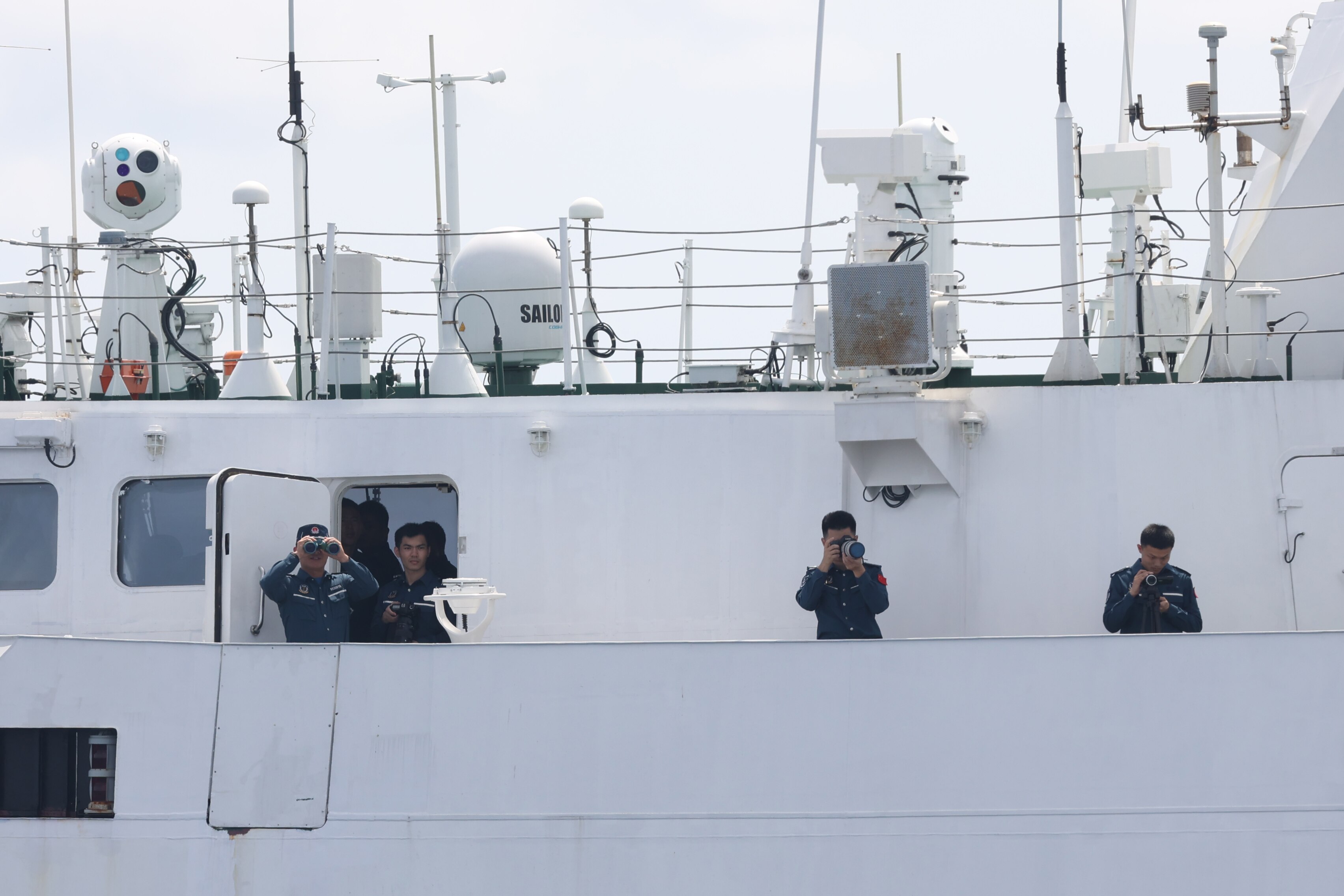 Members of the Chinese Coast Guard photograph Filipino fishermen and media observers on the side of their ship