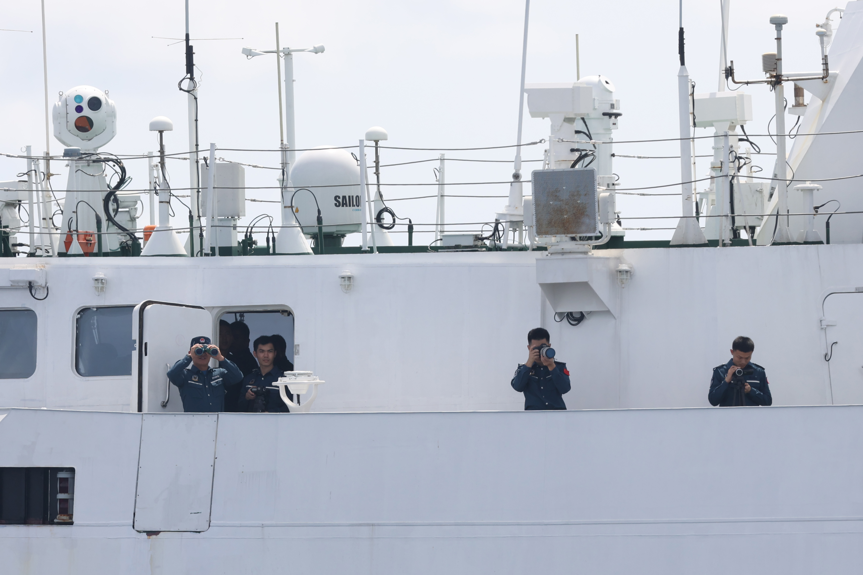 Members of the Chinese Coast Guard photograph Filipino fishermen and media observers on the side of their ship