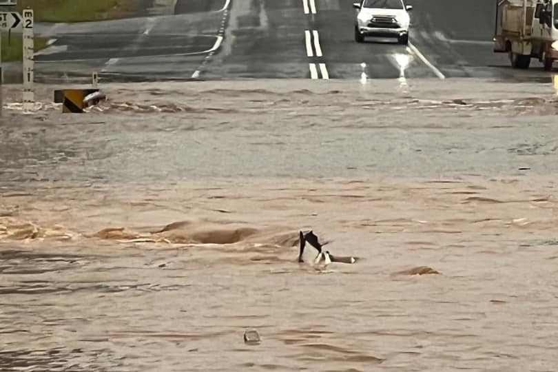 road deeply sumbmerged in water, a car with headlights sits at the edge of the water