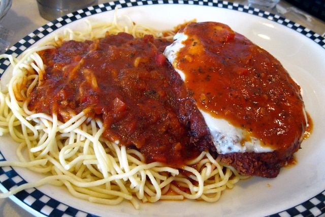 A crumbed chicken fillet with cheese on top on a bed of spaghetti on a giant plate — all covered with red tomato sauce.