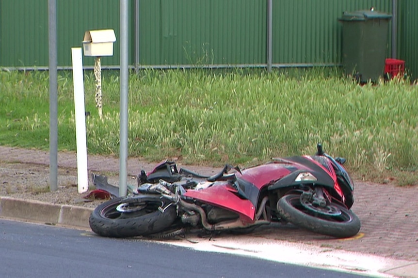 A red motorcycle lying on the ground next to a pole