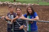 Samara Cassidy with her children Beau and Jordan lean on a gate with sheep in a pen at their property.