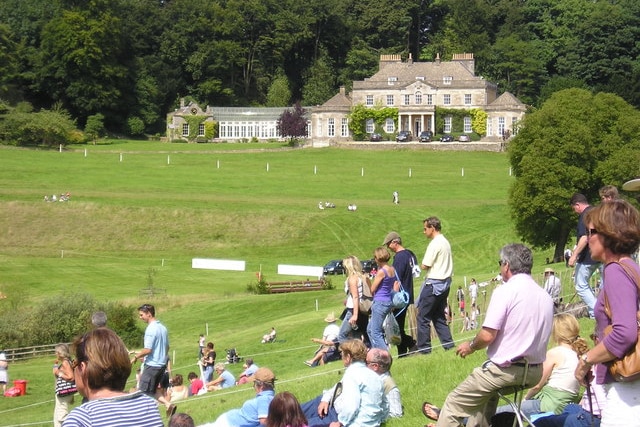 People sit on a grassy hill in front of an old stone house. 