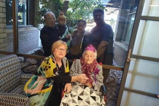 Two people sitting in front of a window with four people standing behind the window looking at the camera.