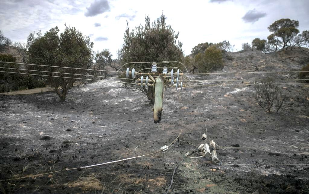 Líneas eléctricas dañadas por el fuego en un paisaje quemado.