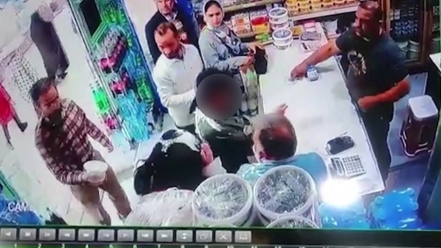 A still image from a security camera in a store when a man confronts two women and throws yoghurt on their hair.