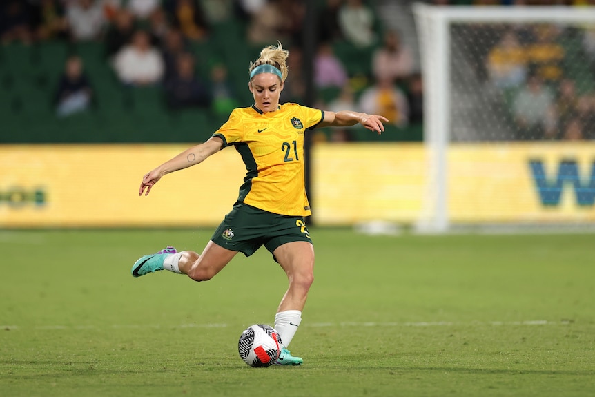 Ellie Carpenter kicks a coccer ball wearing a green and gold uniform.