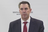 a man in a business suit and red tie speaking in front of sa police banner