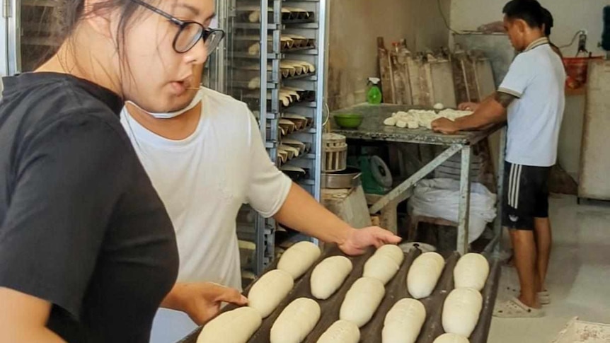 Woman assisting with tray of unbaked banh mi bread rolls.