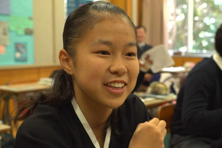 Chong Soni sits at her desk and smiles as she looks past the camera and talks about life at school.