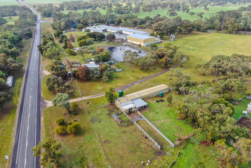 Aerial photo of a couple of school buildings and large basketball court surrounded by green farmland.