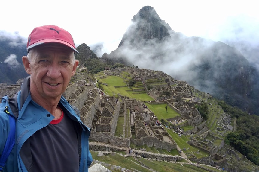 A man in a red cap in a selfie pic with the ancient ruins of Machu Picchu in the background.