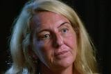 A portrait of a woman with long blond hair in a black room.