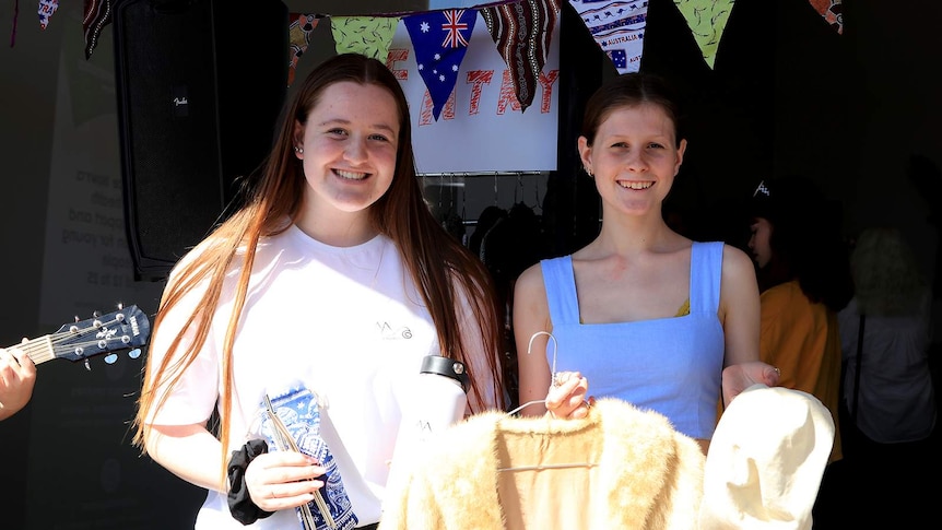 Two teenage girls holding items they sold at their market stalls