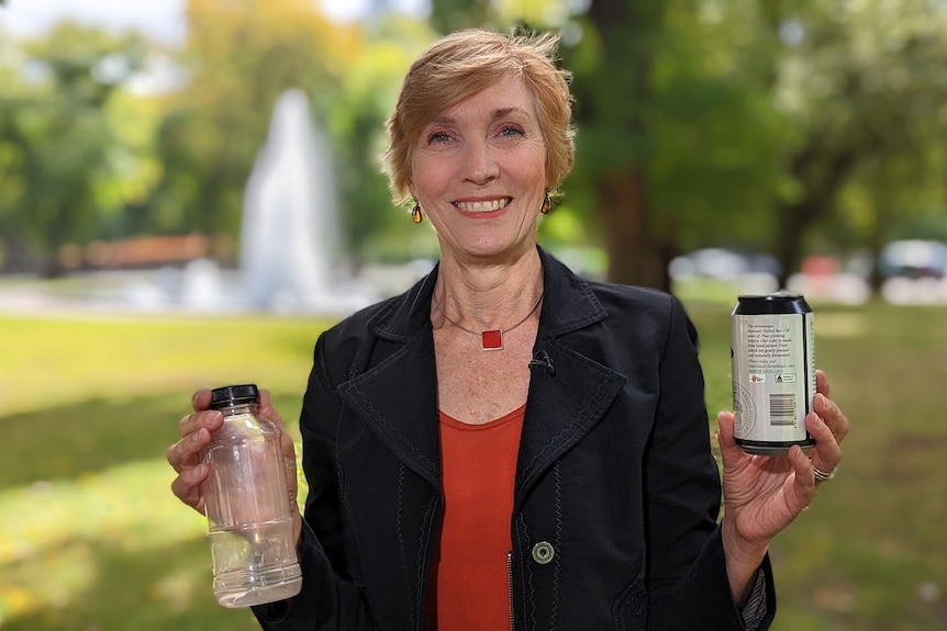 Helen Millicer smiles at the camera, holding up a plastic bottle and a tin.