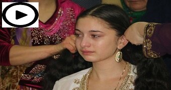 A teenage Roma gypsy girl cries as older women braid her hair.