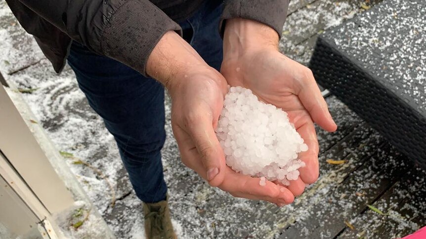 A person holds their hands out with hail stones morphed into a snow ball.