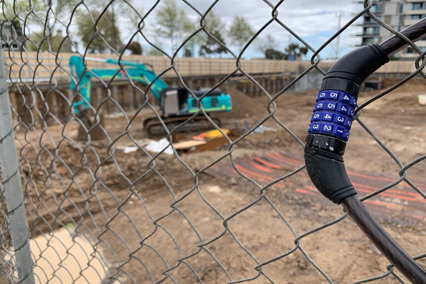 A closed construction site, seen through a chain link fence with a bike lock hanging off it